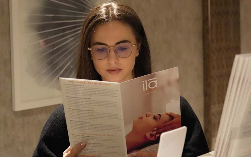 Guest reading ila Only Spa wellness brochure at reception desk in Midtown Manhattan NYC